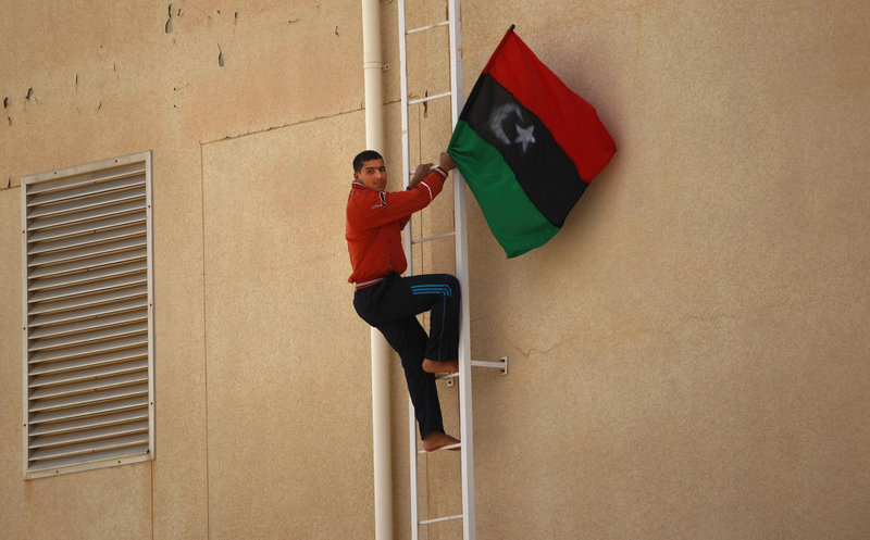 A Libyan rebel climbs to put a pre-Moammar Gadhafi flag on the roof of a government building after fighting against troops in the oil town of Ras Lanouf on Saturday.