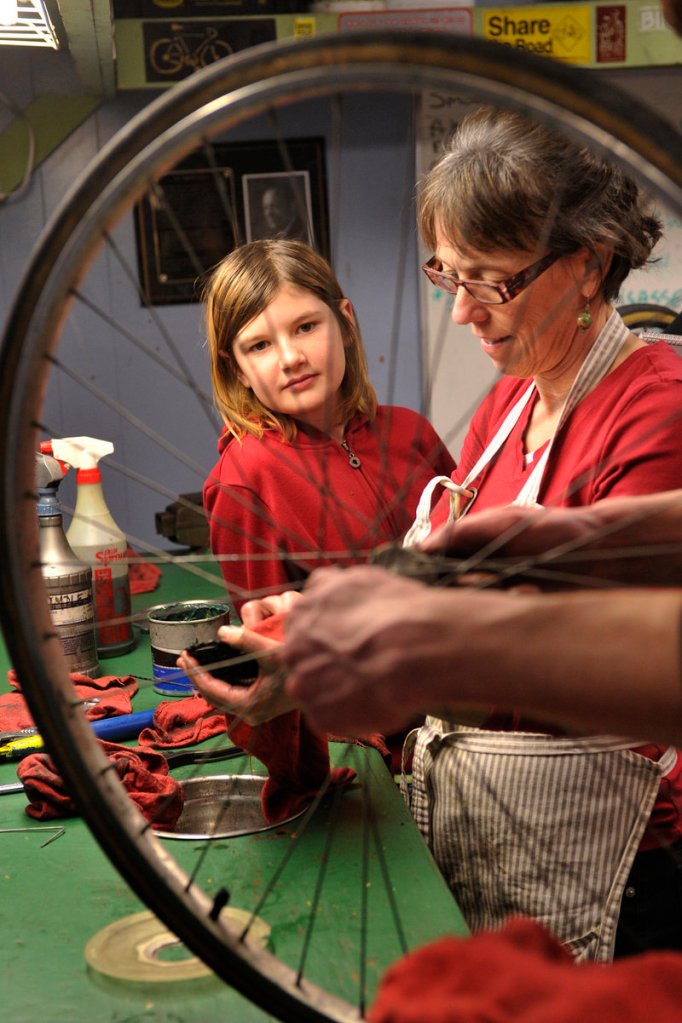 Sophia Hibbard, left, of Windham, and volunteer Karen Nelson are framed by a wheel as they work on a rear hub assembly.