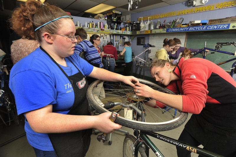 Casey Daigle, left, of Sanford, and Bronwyn Pottoff, who works at the Community Bicycle Center, work on the rear hub of a bicycle.