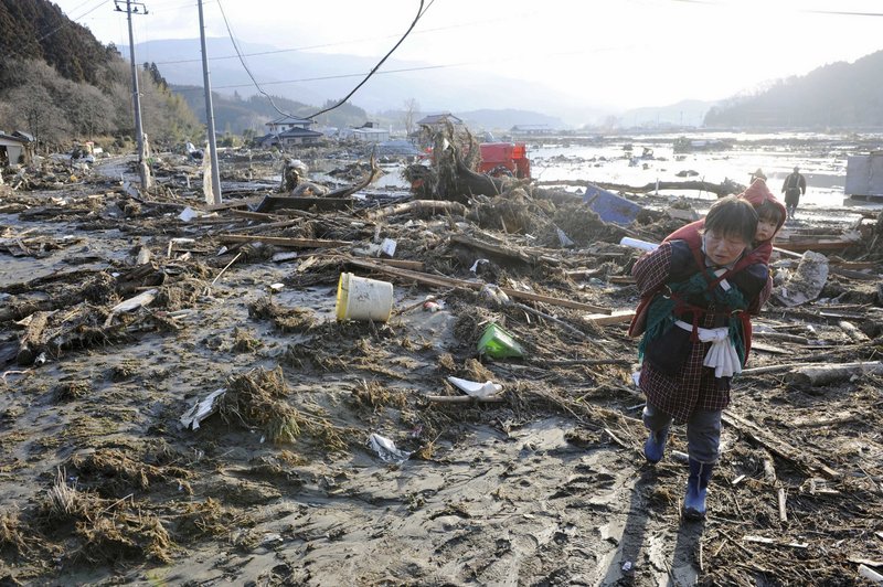 A woman carrying a child walks over debris left by a tsunami that was spawned by the largest earthquake ever recorded in Japan’s history.
