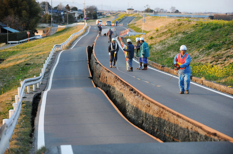 Workers inspect a caved-in section of a prefectural road in Satte, Saitama Prefecture, on Friday.