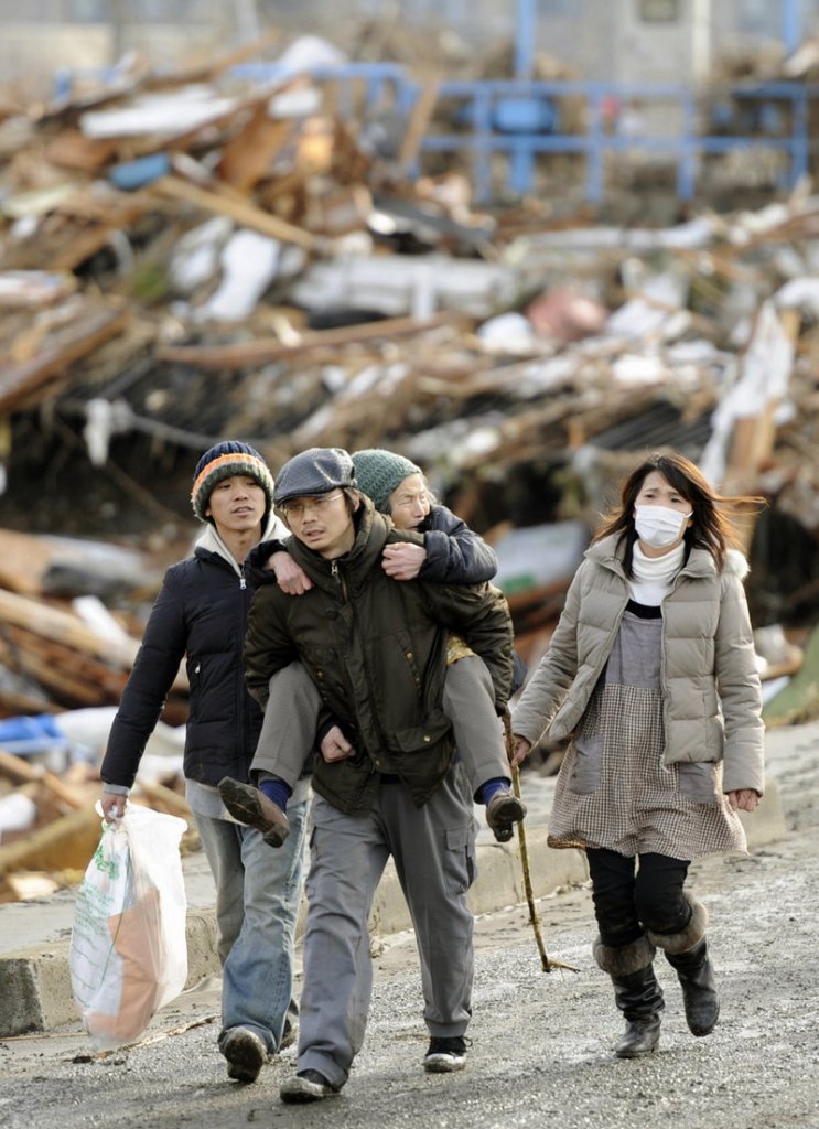 A family walks past flattened houses in Sendai, Miyagi Prefecture on Saturday morning, after Japan’s strongest recorded earthquake slammed its eastern coast Friday.