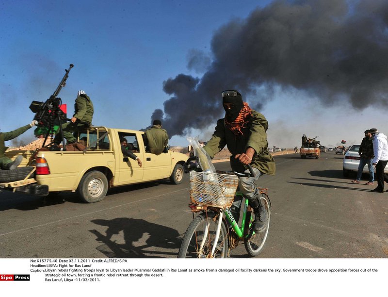Libyan rebels fire on troops loyal to Libyan leader Moammar Gadhafi in Ras Lanuf as smoke from a damaged oil facility darkens the sky. Government troops drove opposition forces out of the strategic oil town, forcing a frantic rebel retreat through the desert.