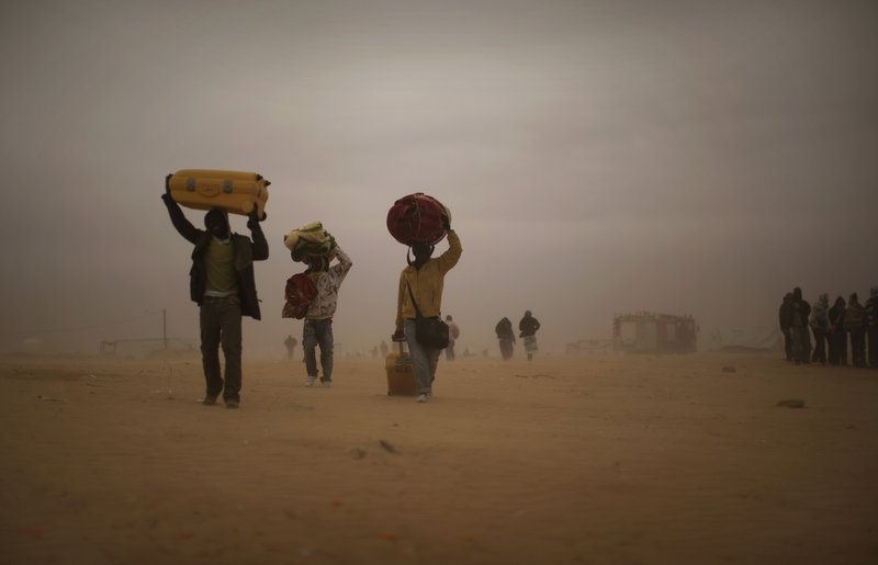 Migrant workers fleeing the unrest in Libya carry their belongings through a sandstorm in a refugee camp in Ras Ajdir, Tunisia, on Tuesday. More than 250,000 migrant workers have left Libya in the past three weeks.