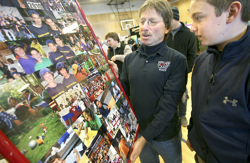 Steve Lepler, director of the West End House Camp in East Parsonsfield, holds a photo collage at Sunday’s camp fair so Alex Smith, 12, of Portland can look for friends who attended the camp.