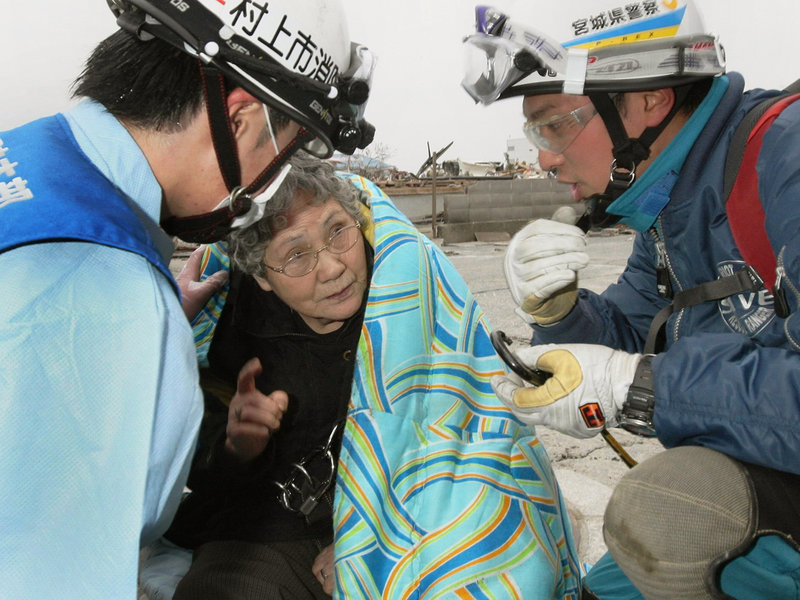 Sumi Abe, 80, speaks to firefighters in Ishinomaki, Miyagi prefecture, in northeastern Japan on Sunday. Abe and her grandson Jin were rescued after the teenager pulled himself out of their flattened house and alerted rescuers.