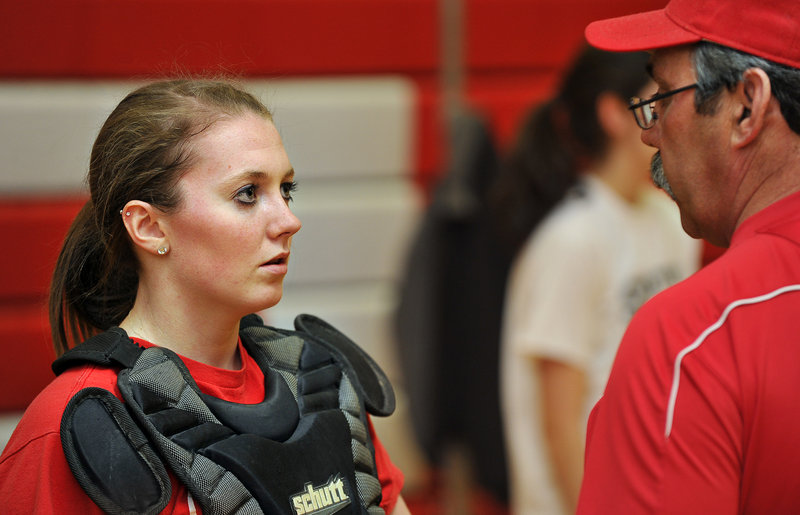 South Portland catcher Katlin Norton listens to instructions from Red Riots softball coach Ralph Aceto on Monday. Pitchers and catchers get a week to limber up before teammates join them for tryouts and practice.