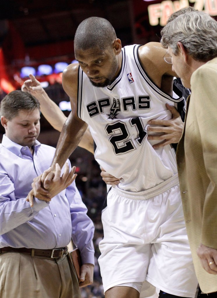 Tim Duncan is helped off the court after spraining his left ankle Monday. He’ll miss at least three games in the Spurs’ stretch drive.