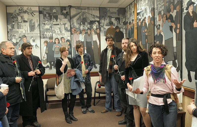 Jessica Graham, right, of Waterville leads a prayer Friday morning in the lobby of the Maine Department of Labor to mark the 100th anniversary of the Triangle Shirtwaist factory fire in New York City, which killed 146 workers. The rally, the first of two Friday to protest the proposed removal of the mural in the background, included the placing of red carnations on a table by the panel depicting the 1937 strike at the Lewiston-Auburn shoe shops.