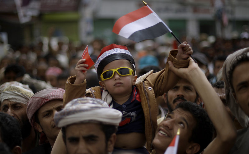 A Yemeni boy waves his national flag Sunday while being lifted by protesters during a demonstration demanding the resignation of President Ali Abdullah Saleh in Sana'a, Yemen. Militants seized control of a weapons factory and a nearby town in Yemen’s south Sunday.