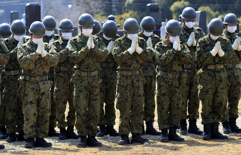 Members of the Japan Ground Self-Defense Force pray Tuesday for victims of the March 11 earthquake at a mass grave site in Yamamoto, in northeastern Japan. With thousands of bodies stored in makeshift morgues, local governments are forced to bury bodies in mass graves.