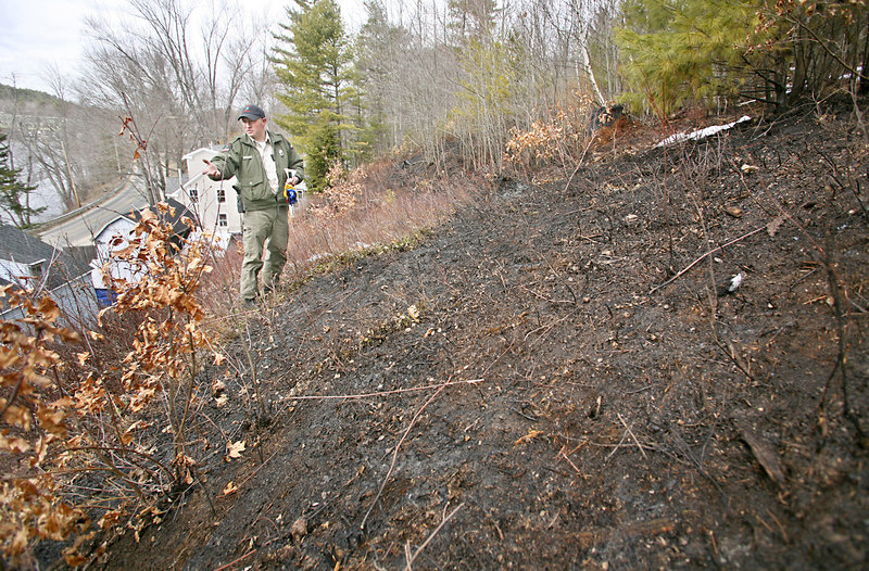 Forest Ranger Matt Bennett investigates the scene of a grass fire that took the life of Frank Hebert, 85, on River Road in Buxton. Hebert was burning grass on an embankment behind his home Wednesday when his clothing caught fire.