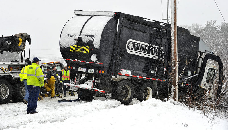 Workers from Pine Tree, the Scarborough fire and police departments and Stewart Towing remove a trash truck from between a utility pole and guardrail at Chamberlain and Pleasant Hill roads in Scarborough.