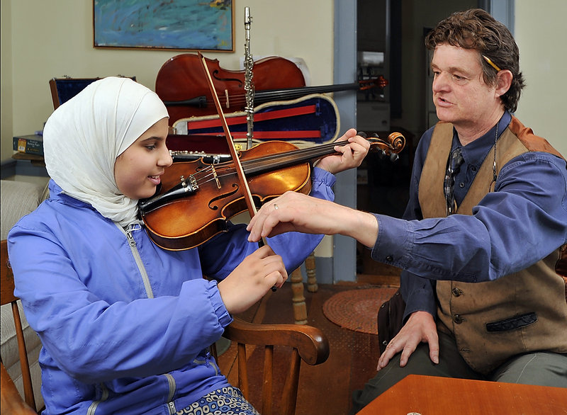 Attorney Peter Lee shows Zahraa Rikan, 15, an Iraqi refugee, how to hold the bow and violin at his office in Yarmouth. Lee collects instruments from donors and loans them to aspiring but cash-strapped kids.