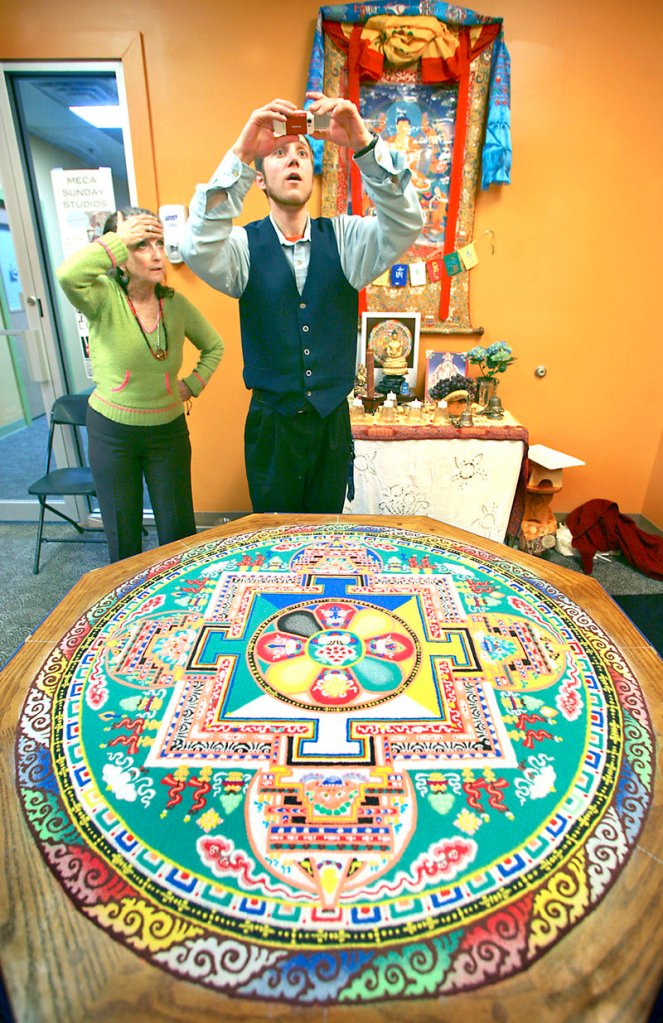 Gerald Pound of Gorham takes a photograph as Louisa-Lora Somlyo of Portland looks on before the deconstruction ceremony of a sand mandala on Sunday.