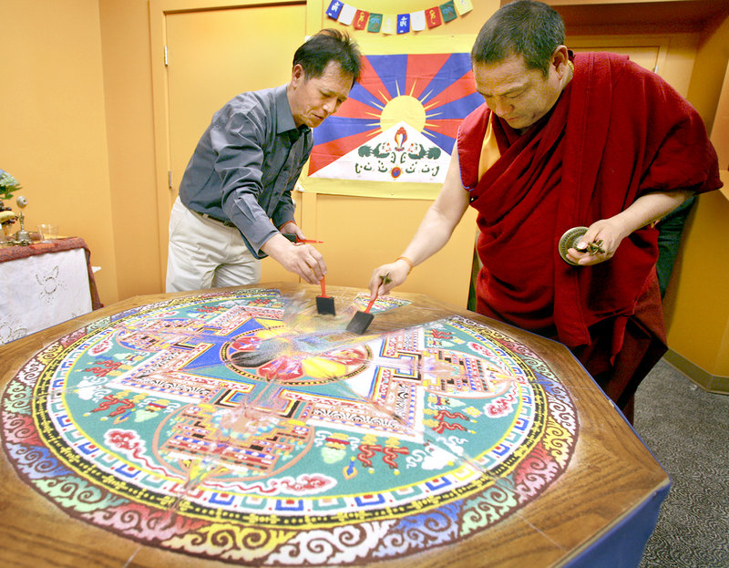 Former Tibetan Buddhist monk Sonam Dhargye, left, and Tibetan Buddhist monk Geshe Gendun Gyatso sweep up sand on Sunday during the deconstruction ceremony of a sand mandala that they created. The mandala was created last week by Tibetan Buddhist monks at the Maine College of Art in Portland.