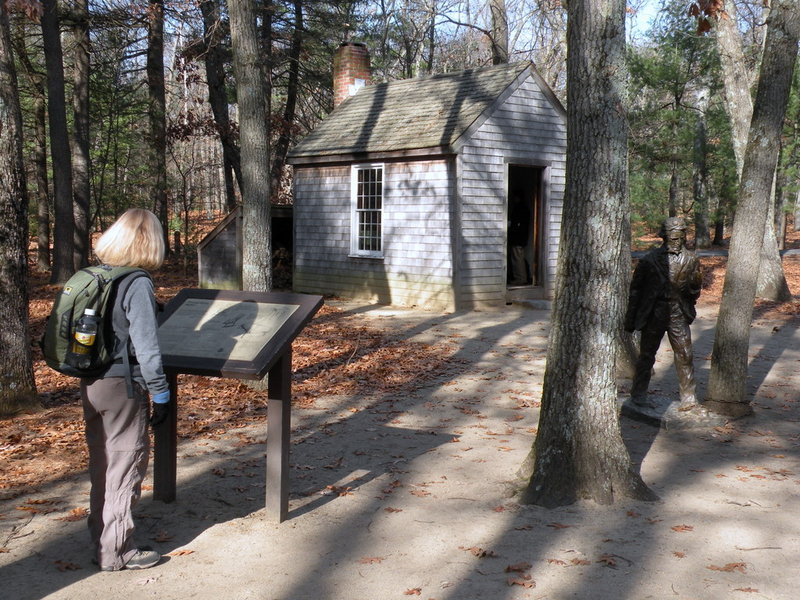 A bronze statue of Thoreau stands in front of a replica of his cabin at Walden Pond State Reservation.