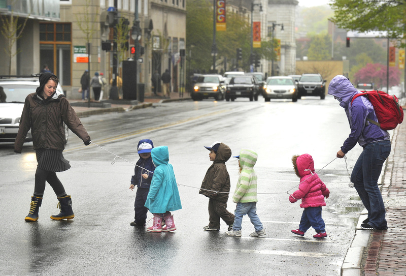 Teachers at the Youth and Family Outreach day care center lead some of their preschoolers across Congress Street on a dark and drizzly Monday morning after a walk around downtown Portland.