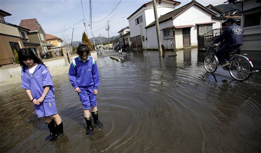 In this May 3, 2011, photo, Itsuki Mogi, 11, left, and and Umi Mogi, 12, watch the moving sea water in a street in front of their house in Ishinomaki, Miyagi Prefecture, Japan. The area in this part of the city sunk nearly 2 feet 7 inches (0.8 meter) following the March 11 earthquake and tsunami.