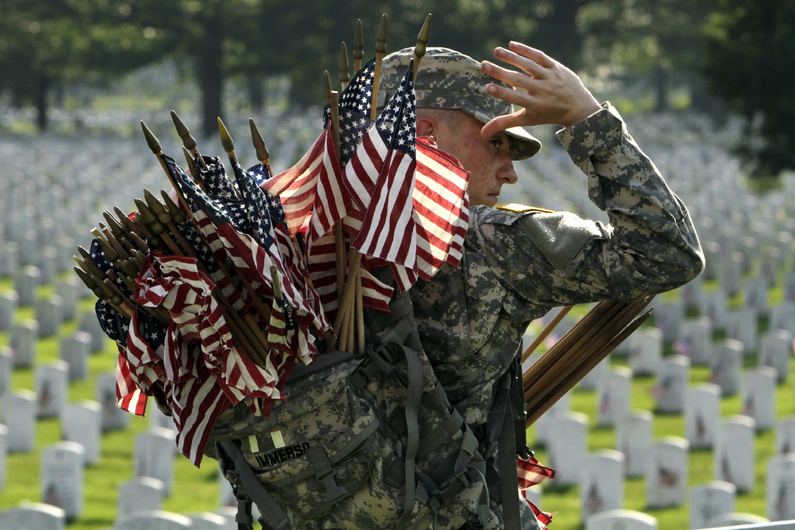 Army Spc. Justin Immerso reaches for a flag to place in front of a head stone at Arlington National Cemetery in Arlington, Va., in preparation for Memorial Day. Every year, on the last Monday in May, Americans pause to pay respect to the men and women who have died while serving their nation in the military.
