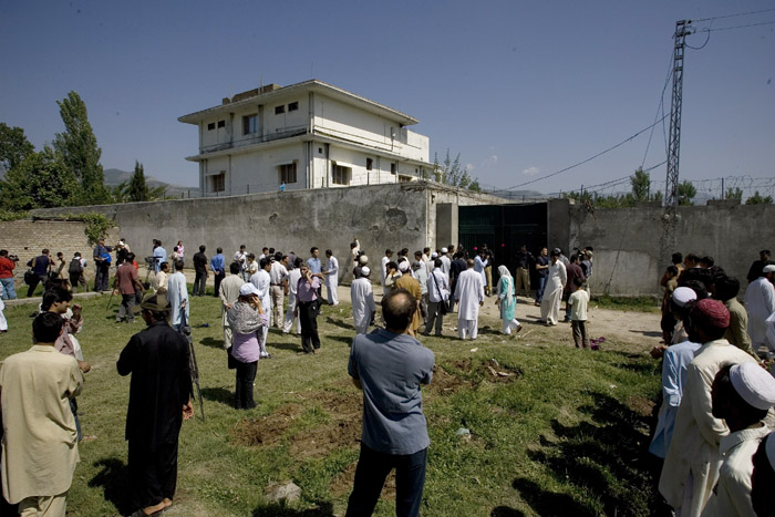 In this photo take Tuesday, local people and media gather outside the perimeter wall and sealed gate of the compound where Osama bin Laden was killed.