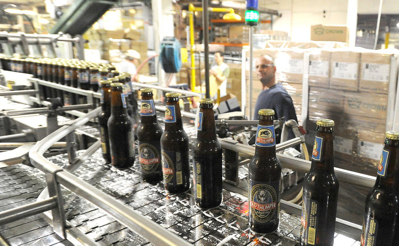Just-filled bottles of Old Thumper file past an employee at Shipyard Brewing in Portland. About 15 types of beer are made under the Shipyard brand.