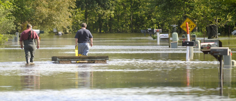 Jeff and Steve Walters float a makeshift platform on Tuesday, trying to save items from a family house in Metropolis, Ill. The Walters had stacked a three-foot sandbag wall around the house, but rising waters overtook it on Monday.
