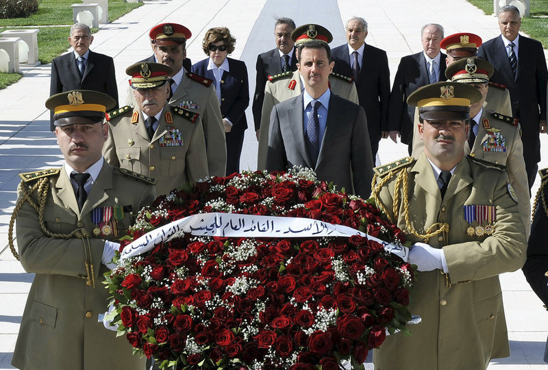 Syrian President Bashar Assad, center in blue tie, arrives to lay a wreath at the tomb of the unknown soldier during Martyr’s Day in Damascus on Friday. Syrian anti-regime protesters again took to the streets across the country on Friday; dozens were slain by security forces.