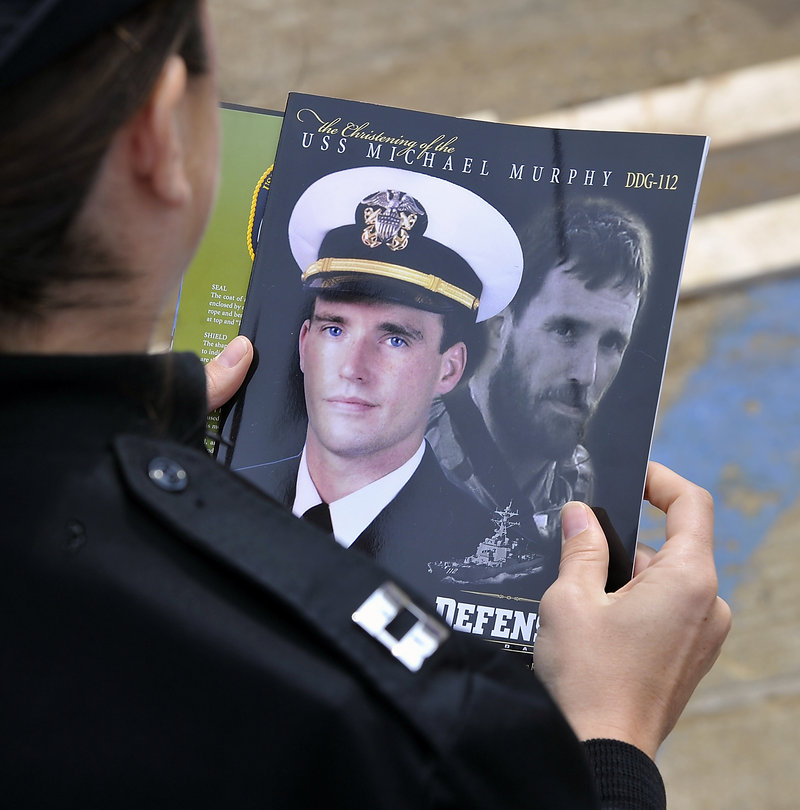 A Navy officer reads the christening program, adorned with images of Lt. Michael Murphy, who is featured in the book “Lone Survivor” by Petty Officer Marcus Luttrell, also a Navy SEAL.