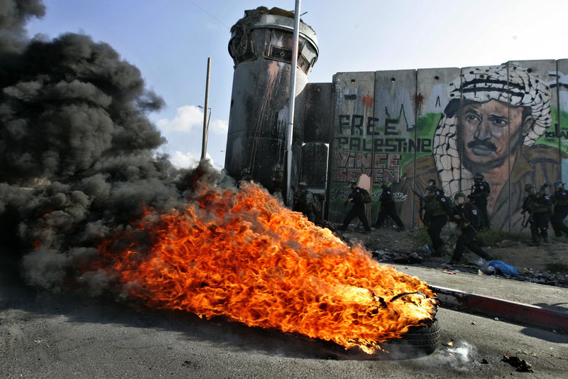 Israeli soldiers run past burning tires under a mural of the late Palestinian leader Yasser Arafat during clashes with Palestinian stone throwers at the Qalandia checkpoint between Ramallah and Jerusalem on Saturday.