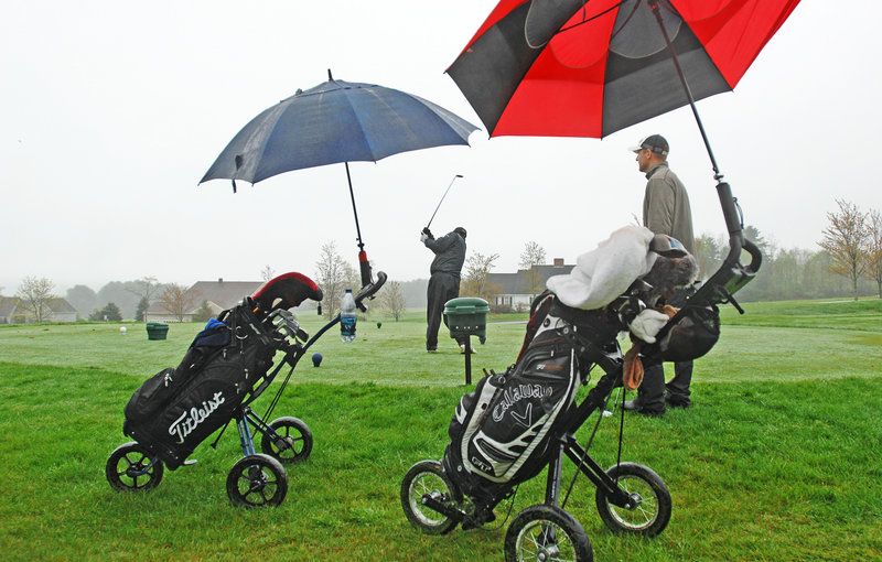 Frank Neuts of Portland hits a shot as Travis Ferrante watches Wednesday at a soggy Falmouth Country Club. They enjoy playing golf in the rain, Ferrante said.