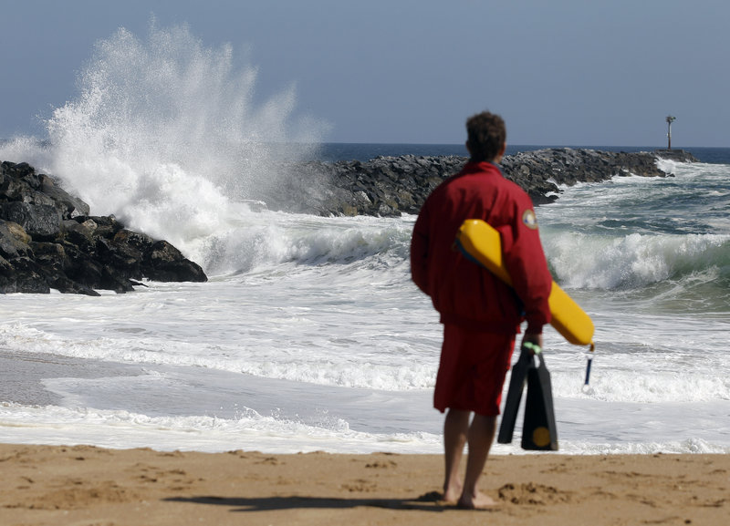 A Newport Beach lifeguard watches the high surf at the “Wedge” in Newport Beach, Calif. The local newspaper recently editorialized about high lifeguard salaries, benefits and overtime pay.