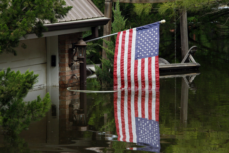 A U.S. flag reflects off the Mississippi River floodwaters in Vicksburg, Miss., on Friday. “We will come HOME,” said one sign in a Louisiana town.