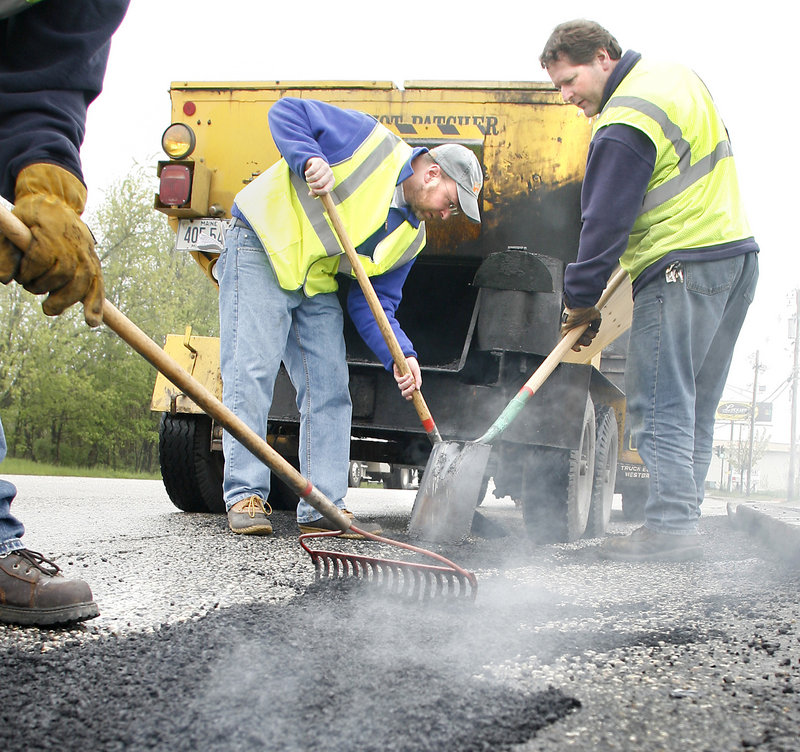 Steam rises as Ray Routhier, center, and city worker Brian Parent fill in one of the many Portland potholes.