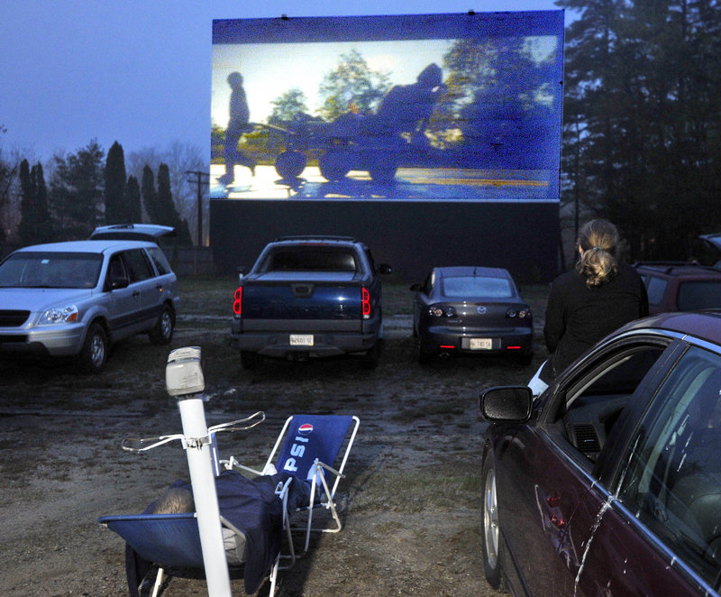 Anne Libby, 15, sits on the hood of her father’s car, right, while her brother lounges in a chair as they watch a movie at the Prides Corner Drive-In in Westbrook. Movies are projected from a reel that measures nearly 3 feet across.