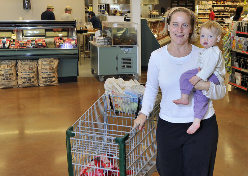 Caroline Loder, newly arrived from Germany and carrying daughter Savanah, 1, at the Bow Street Market in Freeport, says she is reeling from the cost of feeding her family of five an organic vegetarian diet. Her bill soared from $100 a week in Germany to $300 in Maine.