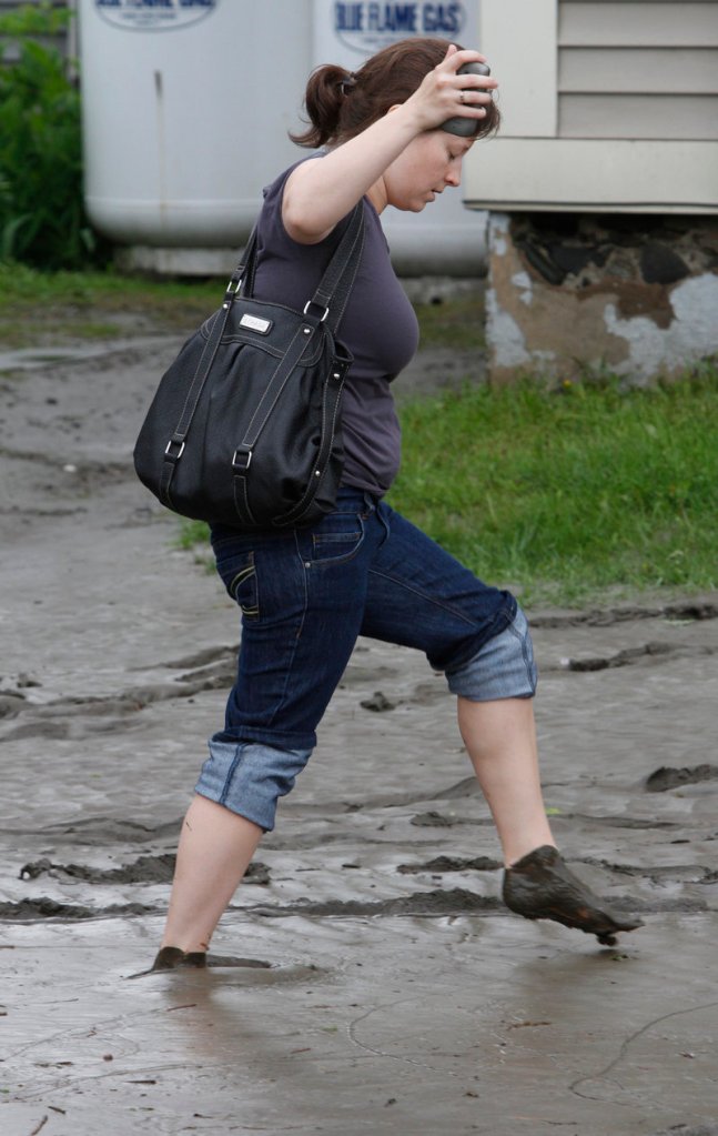 A woman walks on a mud-covered street Friday in Barre, Vt. Roads closed across central Vermont as heavy overnight rains caused rivers to overflow their banks.