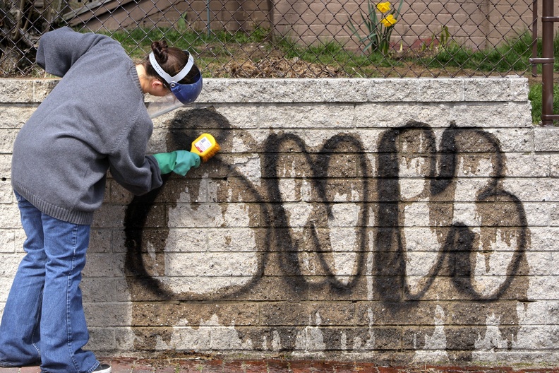 Amanda Fielder, a volunteer, scrubs potassium hydroxide on graffiti on a wall along Moody Street in Portland's Munjoy Hill neighborhood in April. A new graffiti ordinance passed Monday without an escalating system of fines for property owners who fail to remove graffiti after their buildings get “tagged” by vandals.