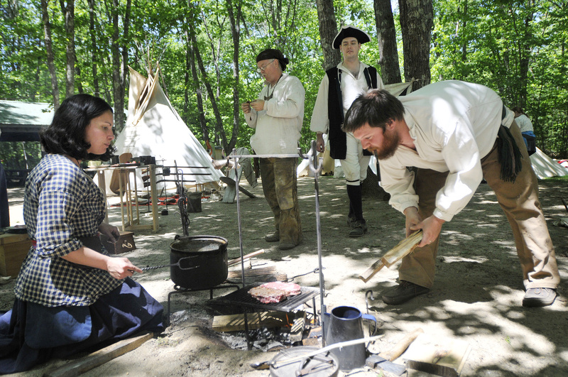 Kurt Priestly of Belmont places split wood on the fire as Renee Grant of Lisbon Falls cooks a steak during the Ancient Ones of Maine camp re-enactment Saturday in Gray.