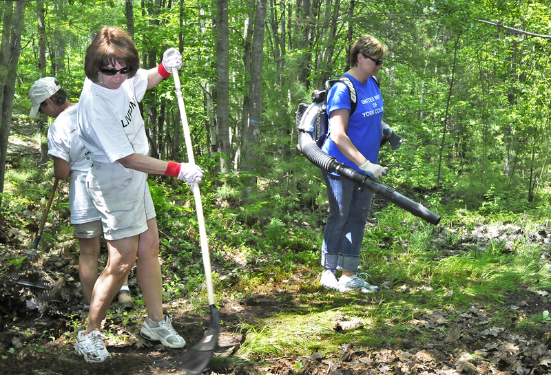 Ellen Murphy rakes while Michelle Sawyer operates a leaf blower during a Day of Caring at the Biddeford YMCA. A crew of about 60 volunteers helped clean up trails, repaint signs and benches, and clear out brush, among numerous other tasks.