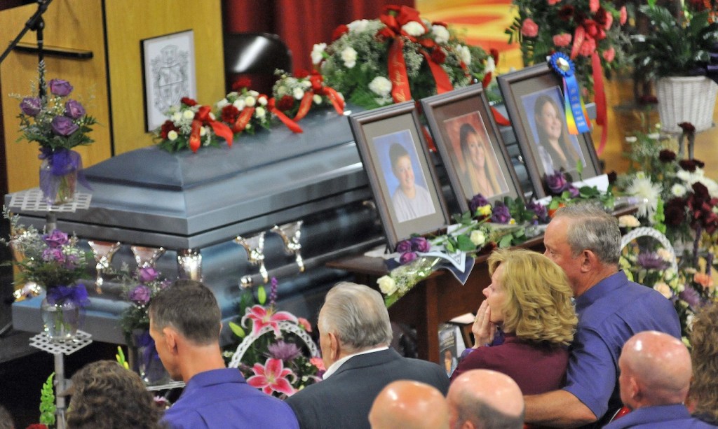 Ralph Bagley, far right, holds his wife Linda as they sit in front of the casket that holds their daughter Amy and grandchildren, Coty and Monica, during the funeral at Dexter Regional High School on Saturday.