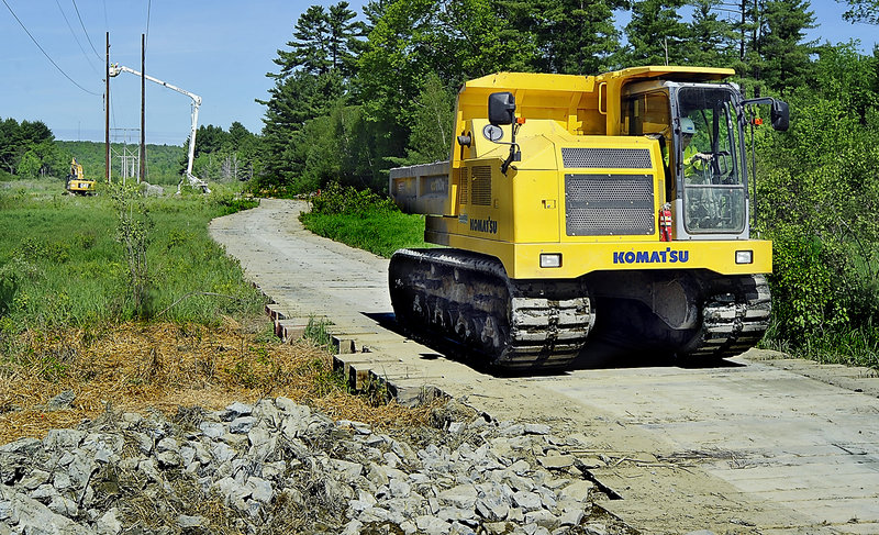 A Komat'su track dump – a specialized dump truck with tractor treads – crosses a wooden mat near a CMP work site.