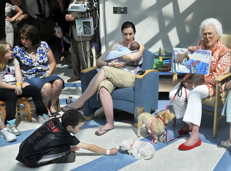 Former first lady Barbara Bush reads to children at Maine Medical Center on Wednesday while Sean Moriarty of Eliot plays with Mrs. Bush’s dogs, Bibi and Mini Me. Mrs. Bush was on hand to read a story to young patients to celebrate her 86th birthday.