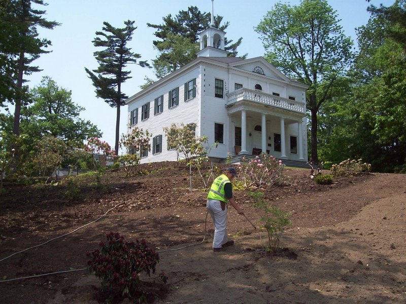 Cyndy Carroll, who works on the landscaping staff at USM Gorham, waters some of the plants at the Joe B. Parks Rhododendron Garden. The 1805 Academy Building, background, is part of the original campus at Gorham, and is now used by the art department.