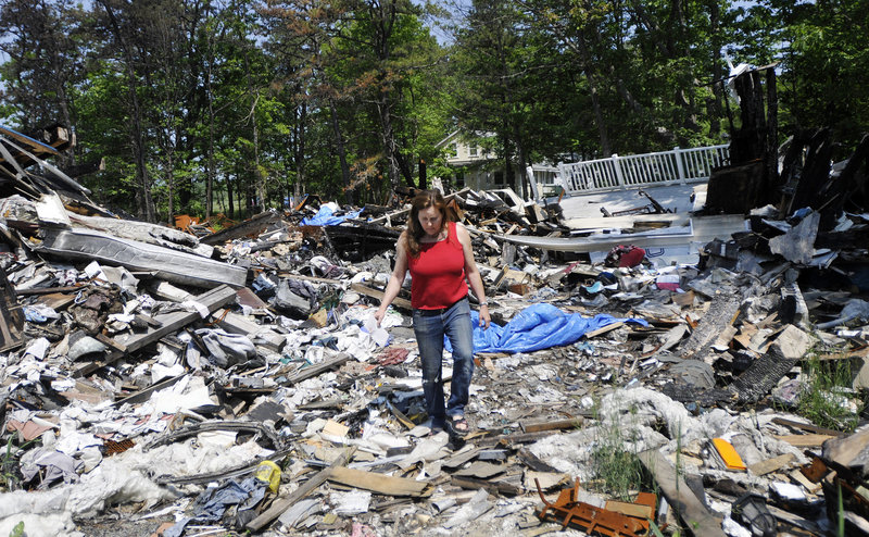 Marcia Lee walks through the rubble of her family’s home at 2 Piney Woods Road in Saco, which burned in February. Lee, who is out of work, and her daughter had just moved in there with her mother, who had lapsed on her homeowner’s insurance and is behind on her taxes.