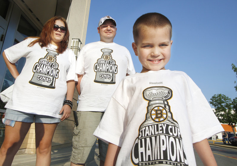 Debi Fields and Chris Lancey of Saco join their 5-year-old son, Aiden, in displaying Bruins pride outside the Maine Mall in South Portland on Thursday. The hockey fans said they bought the last two adult-sized shirts at Olympia Sports in Biddeford and came north to find championship caps.