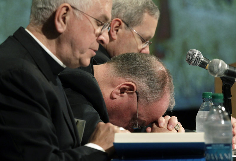 From left, Archbishops Joseph Kurtz and Timothy Dolan, and Monsignor David Malloy bow their heads in prayer as the U.S. Conference of Catholic Bishops’ Spring General Assembly begins Wednesday in Bellevue, Wash.