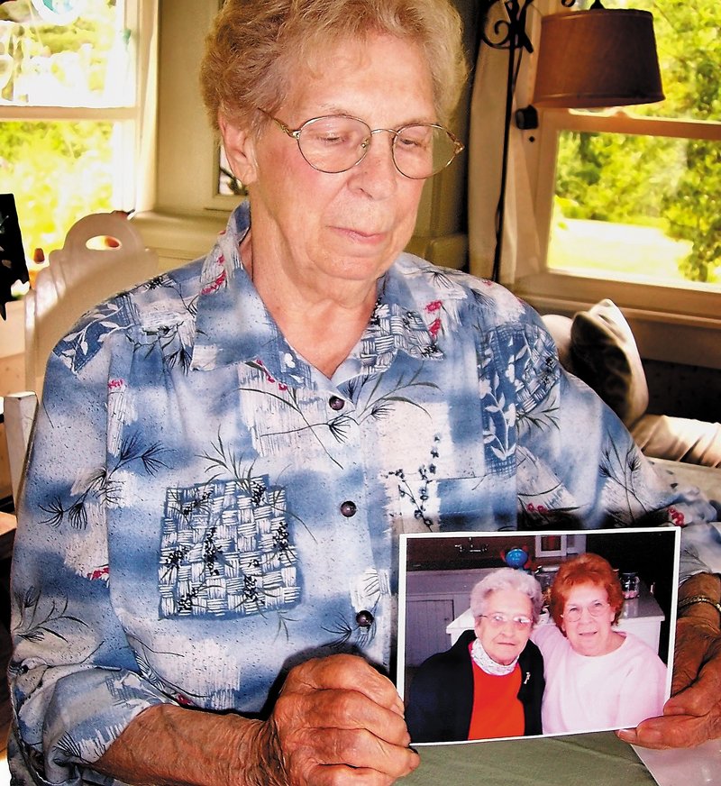 Lois Seamon, 81, sits at her kitchen table with a photo of herself and lifelong friend Grace Burton, 81, who died after being attacked in her Farmington apartment early Tuesday.