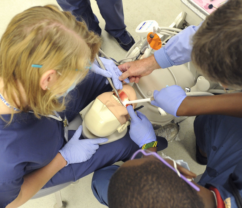 Dr. Lionel Vachon, right, assists Ashlyn Drumm and David Ndayishimiye in drilling a tooth of the patient simulator Monday at UNE’s Dental Careers Exploration Camp.