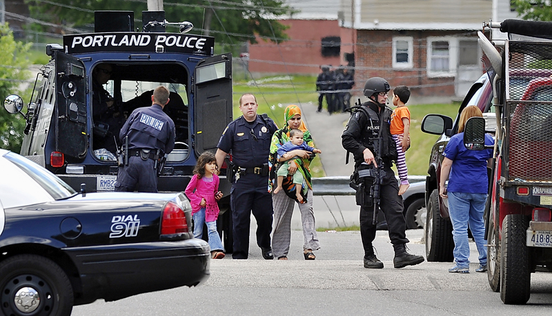 Sgt. Andrew Hutchins, left, helps a young girl, mother and baby as a member of the Portland Police Special Reaction Team carries a young child from the "Peace Keeper" vehicle. The family was being evacuated from a nearby apartment where a standoff was in progress today. Other members of the team are in the background awaiting orders near the standoff situation.